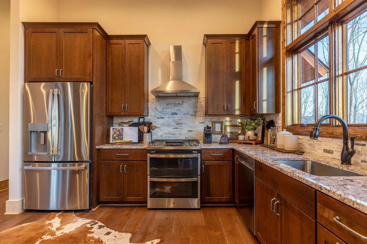 A chef-ready kitchen featuring a stainless steel refrigerator, granite countertop, wooden cabinets, and large windows for ample natural light. The well-equipped space invites cooking, entertaining, and family interaction.