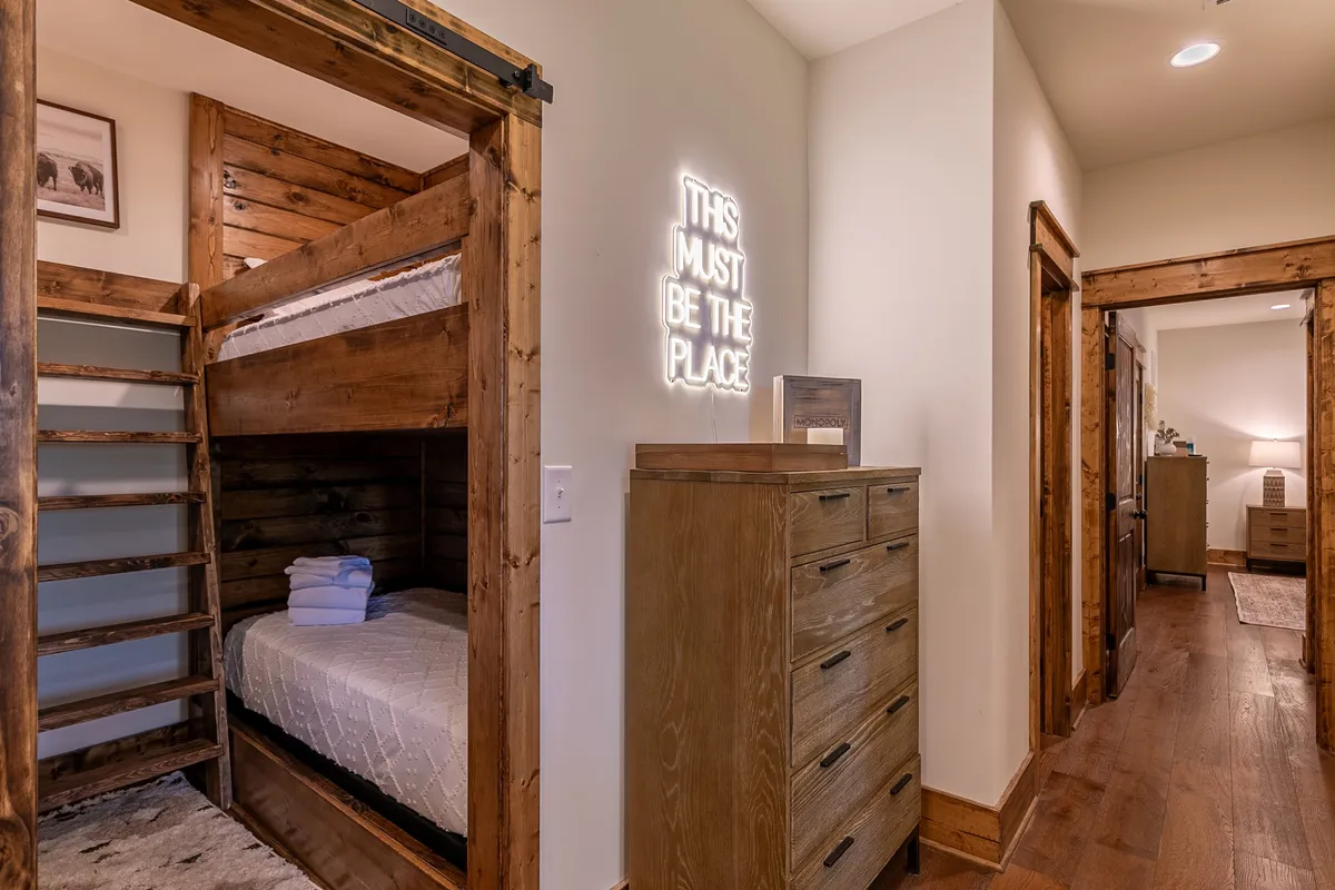 This image displays a bunk room with built-in bunk beds, a neon sign, and a cozy dresser. The beds are made up invitingly, and the space feels cheerful and perfect for kids or teens to relax, read, or have late-night fun.