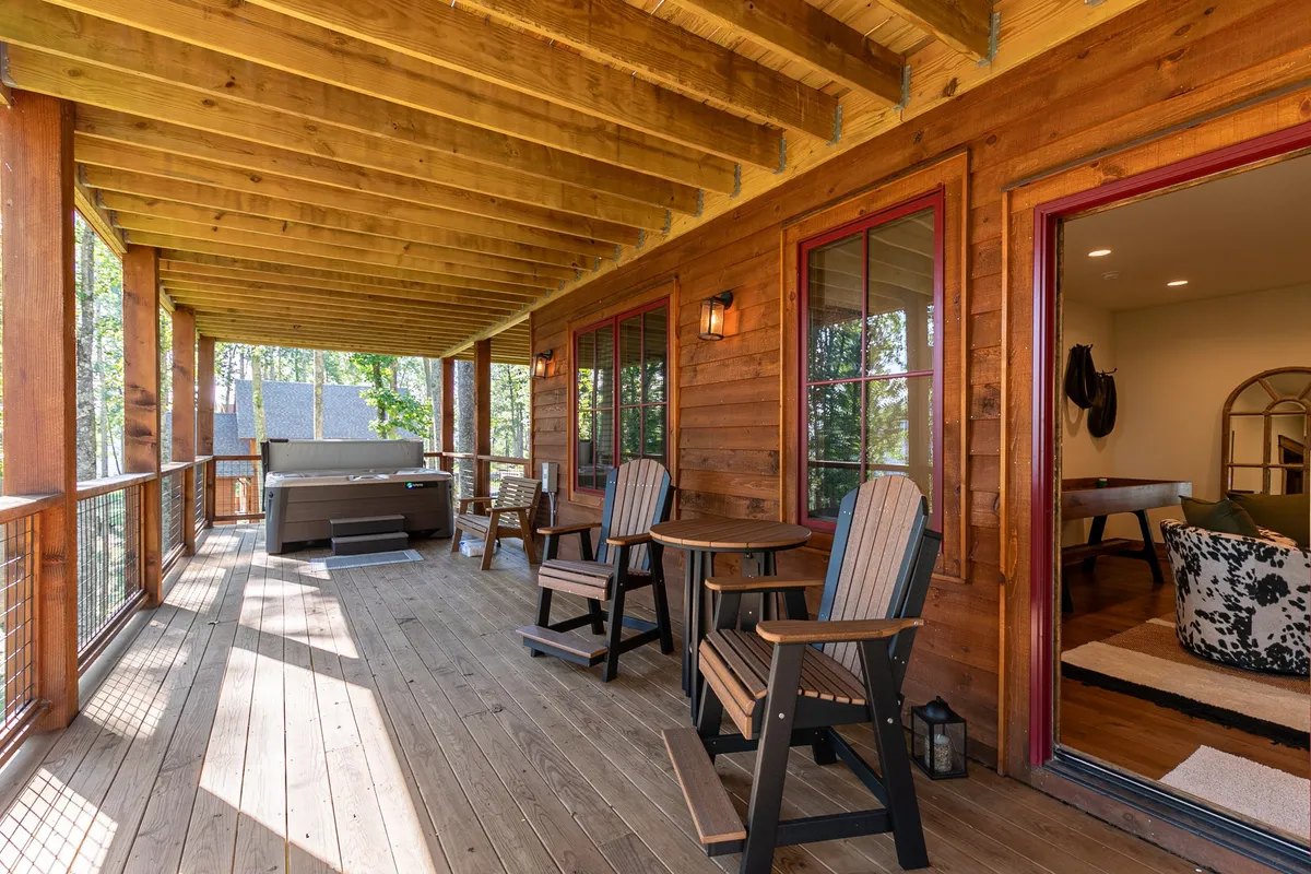 This image features a wooden deck with a hot tub and rocking chairs, set against large windows and surrounded by trees. The scene is tranquil, inviting relaxation and social gatherings while providing a sense of privacy and immersion in nature.