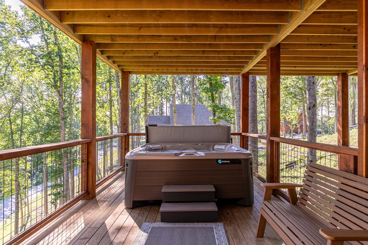 A tranquil exterior setup featuring a private hot tub surrounded by tall trees and a wooden bench, set against a backdrop of natural greenery. The scene suggests relaxation and rejuvenation after a day of active pursuits, with the hot tub as a focal point for unwinding while immersed in nature.