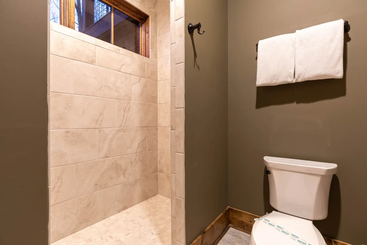 This image features a small but modern bathroom with a glass shower, toilet, fresh towels, and neutral tilework. It's clean, easily accessible, and provides all the essentials for convenience on the lower level.