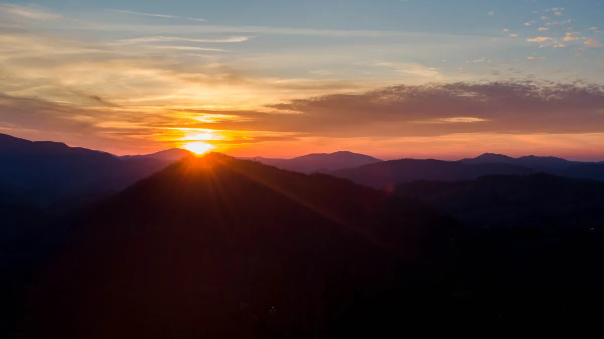This image captures a panoramic sunset over mountain silhouettes, creating a serene and awe-inspiring atmosphere. The fading light invites guests to savor the breathtaking natural beauty and consider evening activities like photography or stargazing.