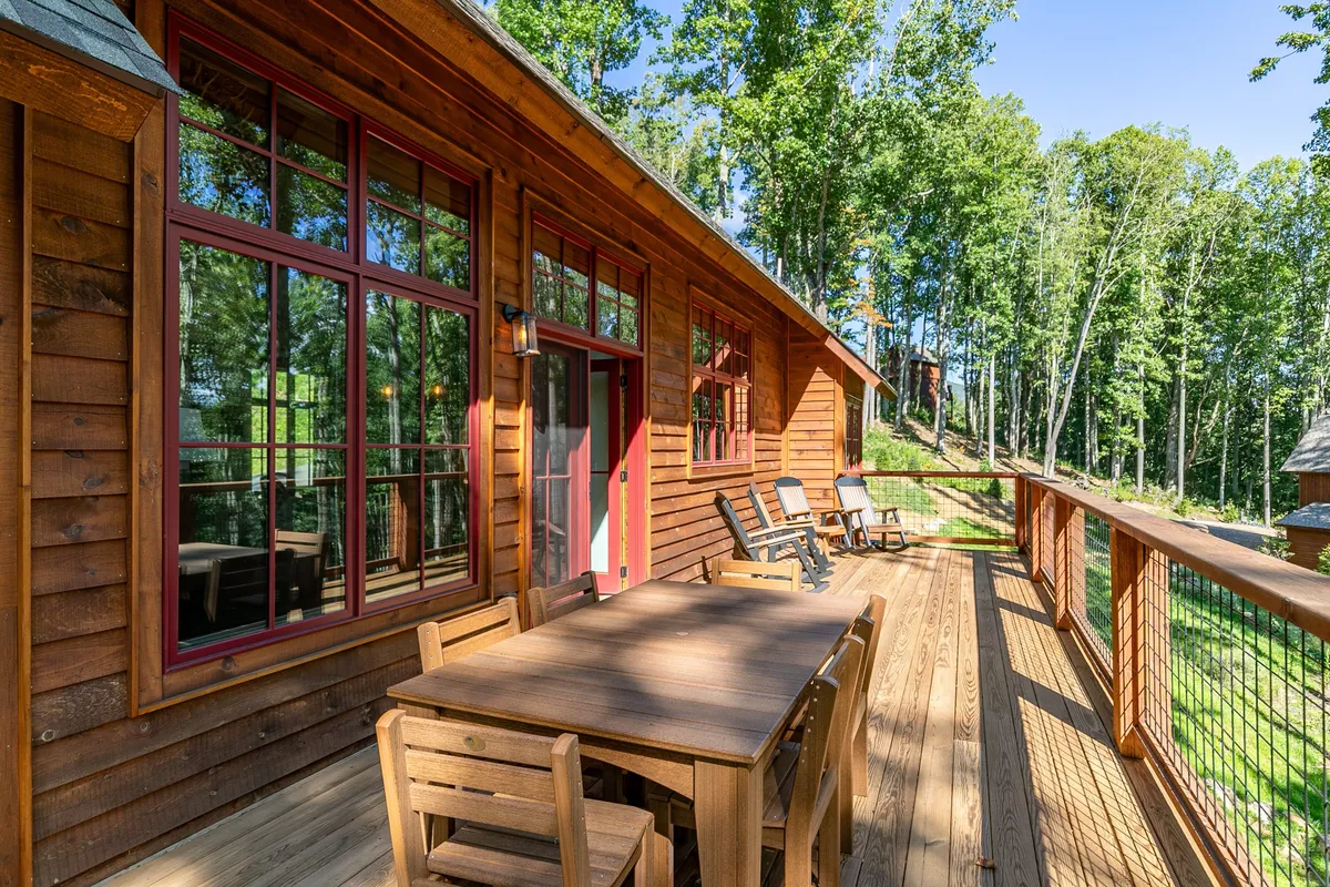 A wooden deck with a dining table surrounded by trees, creating an inviting space for outdoor meals and gatherings. The deck offers a vantage point over the surrounding greenery, evoking a sense of tranquility and connection with nature.