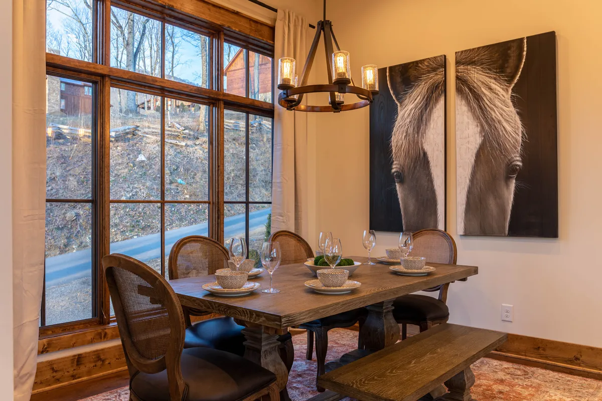 A warm and inviting dining area with a large wooden dining table, elegant chandelier overhead, and equestrian artwork on the wall. The space is set for family meals and celebratory gatherings.