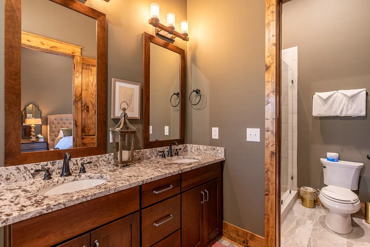 A spa-inspired bathroom with dual granite sinks, large mirrors, decorative lantern, and modern lighting. The space is serene and elegant, perfectly suited for relaxing morning routines or unwinding after a long day.